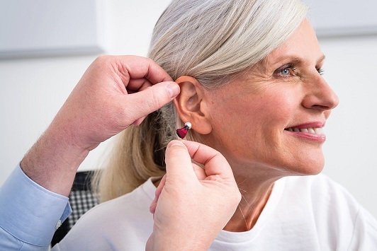 Ältere Frau bekommt ein modernes Hörgerät angepasst, Hörakustiker berät freundlich.